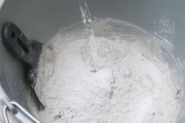 Kovaya beyaz alçıyı karıştırıcı ile karıştırmak. Yakın plan..