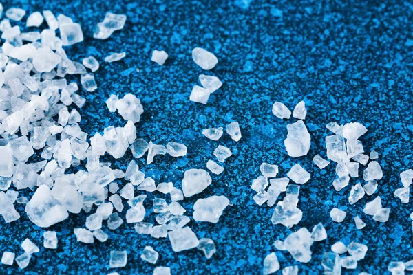 Durva sókristályok a kék asztalon. tengeri só. A sós reklám háttere. — Stock Fotó