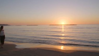 Günbatımı sırasında bir kumsalda yürüyen güzel kadın