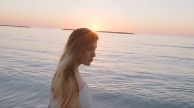 Günbatımı sırasında bir kumsalda yürüyen güzel kadın