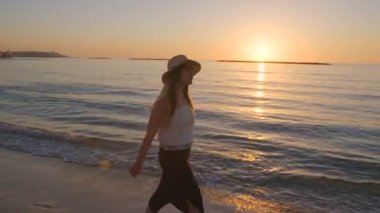 Günbatımı sırasında bir kumsalda yürüyen güzel kadın