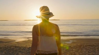 Günbatımı sırasında bir kumsalda yürüyen güzel kadın