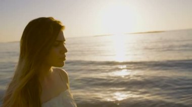 Günbatımı sırasında bir kumsalda yürüyen güzel kadın