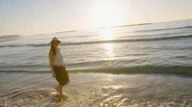 Sahilde günbatımı sırasında yürüyen kadın