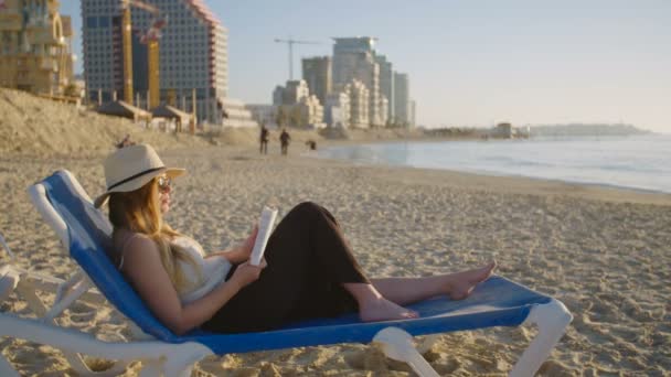 Красива жінка сидить і читає на пляжі — стокове відео