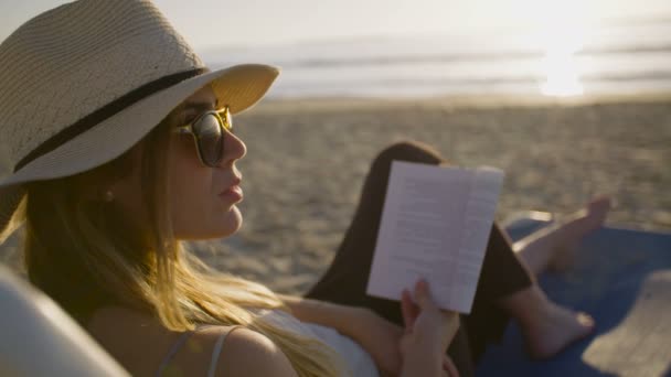 美丽的女人坐在和在海滩上阅读 — 图库视频影像