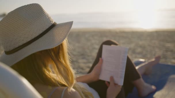 Hermosa mujer sentada y leyendo en la playa — Vídeo de stock