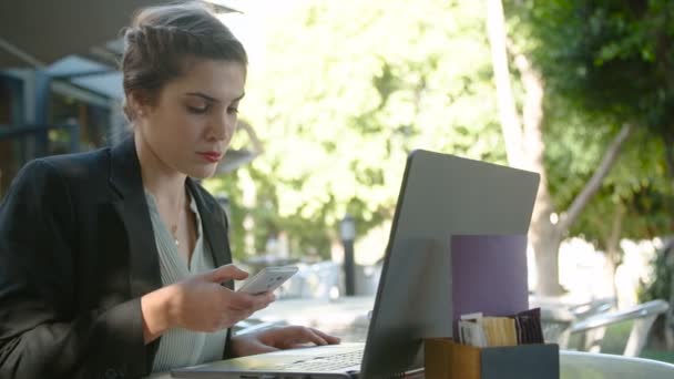 Mulher de negócios trabalhando em um laptop e fazendo chamadas telefônicas — Vídeo de Stock