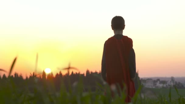 Niño con una capa de superman en un campo durante el atardecer — Vídeo de stock