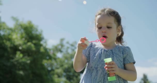 Een klein meisje waait zeep bubbels buitenshuis — Stockvideo