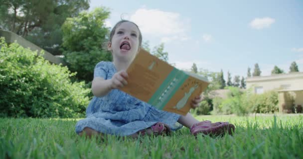 Petite fille lisant un livre pour enfants à l'extérieur — Video