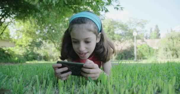 Дівчина грає з мобільним телефоном, що лежить на траві — стокове відео
