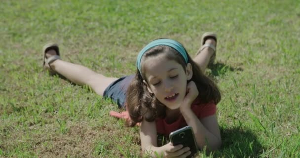 Une fille jouant avec un téléphone portable étendu sur l'herbe 