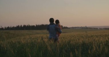 Bir anne ve kızı bir buğday alanında günbatımı sırasında oynamaya
