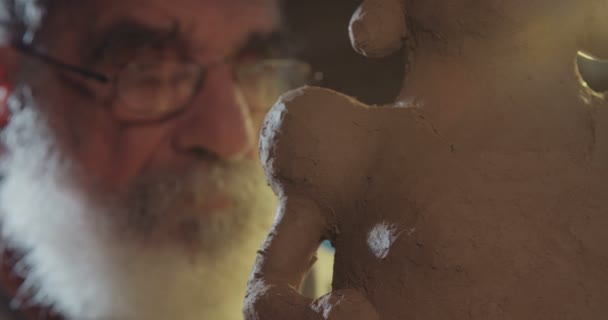 Oude kunstenaar modellen een sculptuur van de klei in een kleine studio — Stockvideo