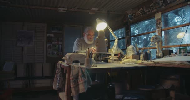 Oude kunstenaar modellen een sculptuur van de klei in een kleine studio — Stockvideo