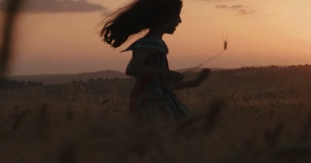 Νεαρό κορίτσι που τρέχει σε ένα πεδίο κατά τη διάρκεια του ηλιοβασιλέματος — Αρχείο Βίντεο
