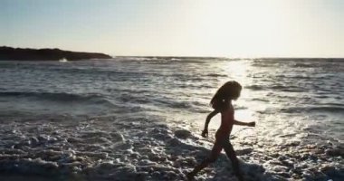 Sahilde günbatımı sırasında mutlu koşan genç kız