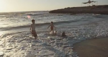 Üç çalışan ve birlikte sahilde günbatımı sırasında oynayan çocuklar