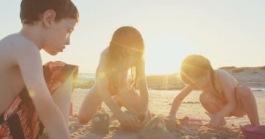 Üç çocuk kumdan kaleler sahilde günbatımı sırasında bina