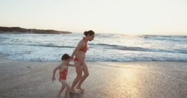 Anne ve kızı kumsalda günbatımında çalışan