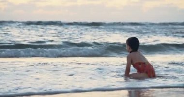 Sahilde dalgaların günbatımı sırasında zevk kum üzerinde oturan küçük kız