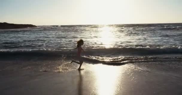 Молодая девушка бежит счастливой на пляже во время заката — стоковое видео