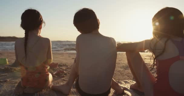 Tres niños comiendo sandías en la playa al atardecer — Vídeos de Stock