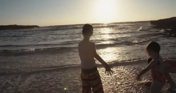 Drie kinderen lopen en spelen samen op het strand tijdens zonsondergang — Stockvideo