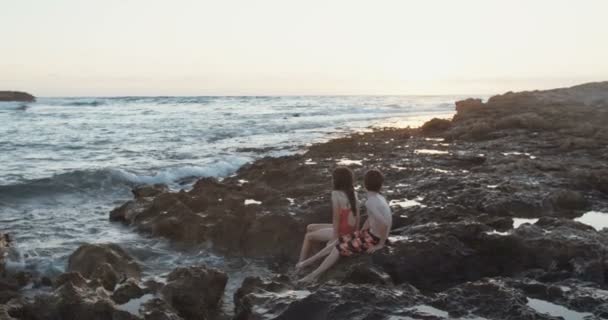 Двоє дітей сидять на пляжі під час заходу сонця — стокове відео