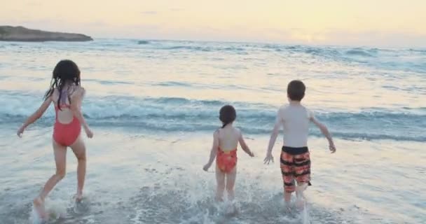 Troje dzieci, działa i gra razem na plaży podczas zachodu słońca — Wideo stockowe
