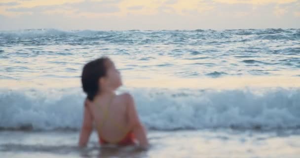 Niña sentada en la arena de la playa disfrutando de las olas al atardecer — Vídeo de stock