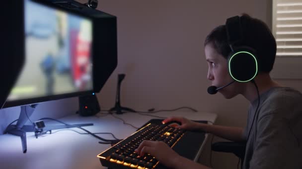 Jonge jongen zittend achter een computer, een spel spelend met een headset — Stockvideo