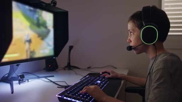 Niño sentado frente a una computadora, jugando a un juego con auriculares — Vídeos de Stock