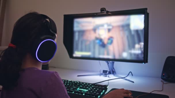 Jong meisje zitten in de voorkant van een computer, het spelen van een spel dragen van een headset — Stockvideo