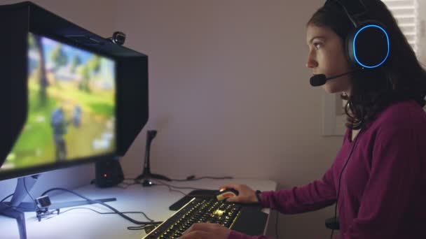 Teenage girl sitting in front of a computer, playing a game wearing a headset — Stock Video