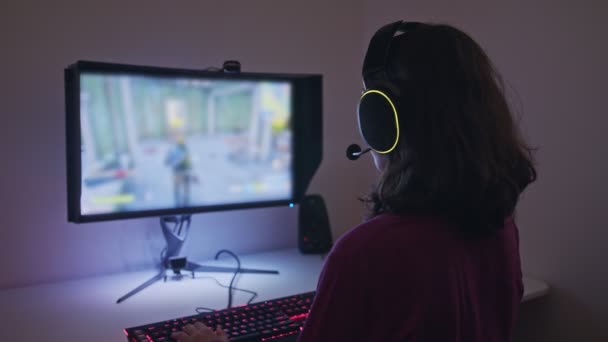 Genç bir kız bilgisayarın önünde oturmuş, kulaklık takarak oyun oynuyor. — Stok video