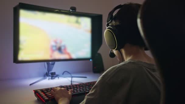 Jonge jongen zittend achter een computer, een spel spelend met een headset — Stockvideo