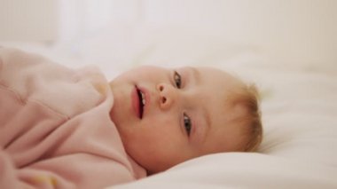 Güzel bir kız bebek yatakta oturuyor, oynuyor, yuvarlanıyor ve gülüyor.