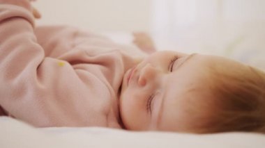 Güzel bir kız bebek yatakta oturuyor, oynuyor, yuvarlanıyor ve gülüyor.