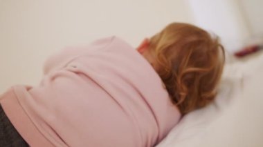 Güzel bir kız bebek yatakta oturuyor, oynuyor, yuvarlanıyor ve gülüyor.