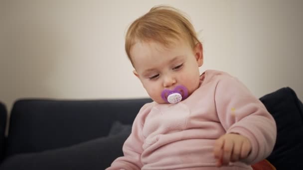 Cute baby girl playing at home with a pacifier in her mouth — Stock Video