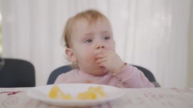 Masanın yanında portakal yiyen şirin bir bebek.