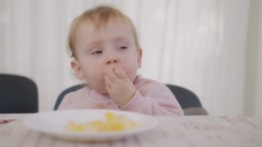 Masanın yanında portakal yiyen şirin bir bebek.