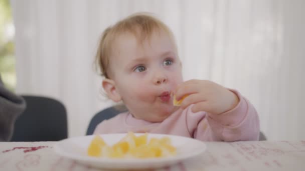 Lindo bebé comiendo una naranja al lado de una mesa — Vídeo de stock