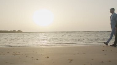 Günbatımında kumsalda birlikte yürüyen eşcinsel çift.