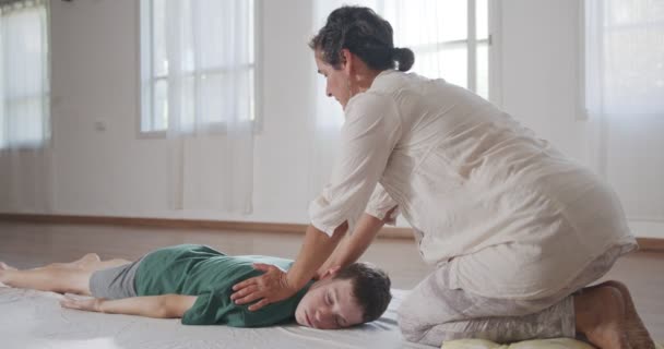 Shiatsu treatment. Masseuse giving treatment to a young boy, pressing on his back and neck — Wideo stockowe