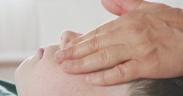 Shiatsu treatment. Masseuse giving a gentle face massage to a young boy — Wideo stockowe