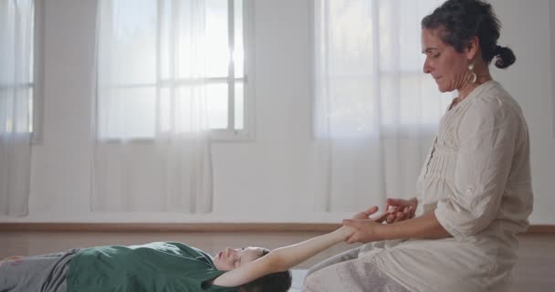 Shiatsu treatment. Masseuse giving treatment to a young boy, pressing on his back and neck — Wideo stockowe