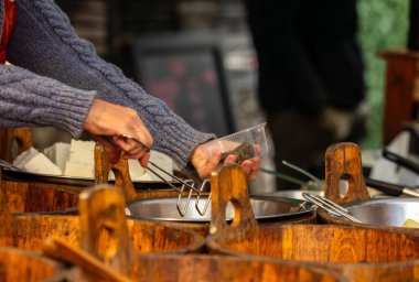 Market vendor handling food at outdoor stall with wooden barrels and serving utensils.